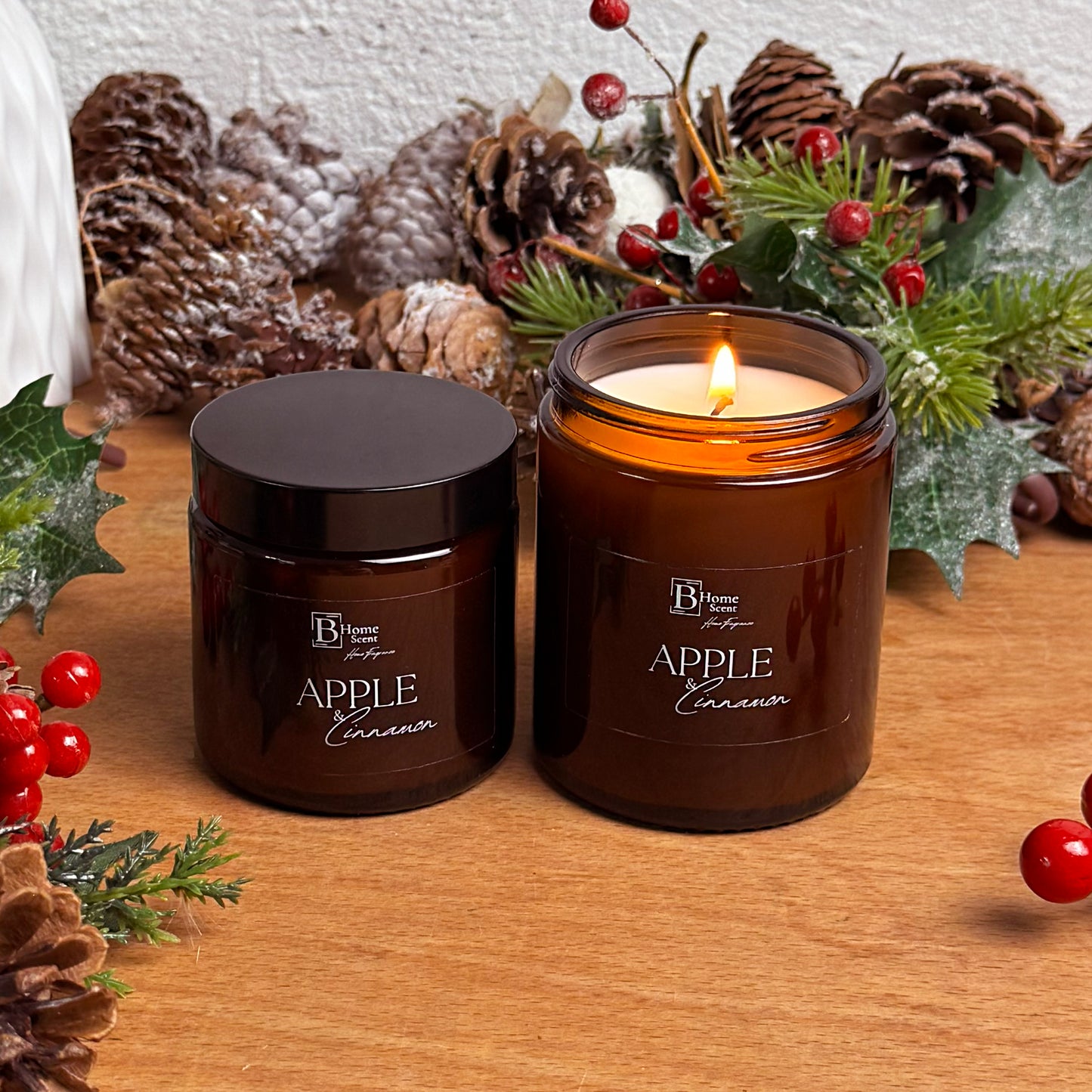 small and medium Lit Apple and Cinnamon Christmas candles in an amber glass jar surrounded by pinecones and holiday décor.
