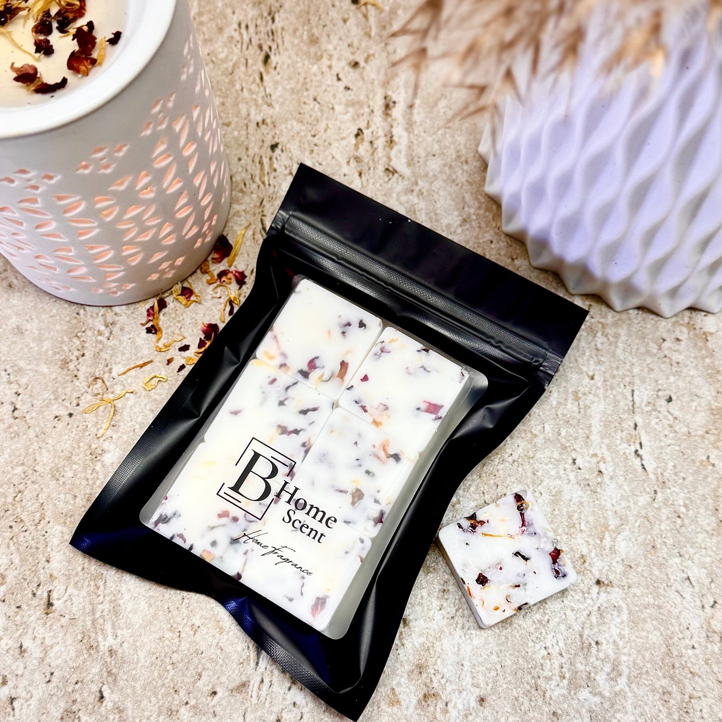Pineapple Peach Sangria Botanical Wax Melt Bar with Dried Petals in Black Resealable Pouch, Shown Beside Ceramic Wax Burner on Stone Surface