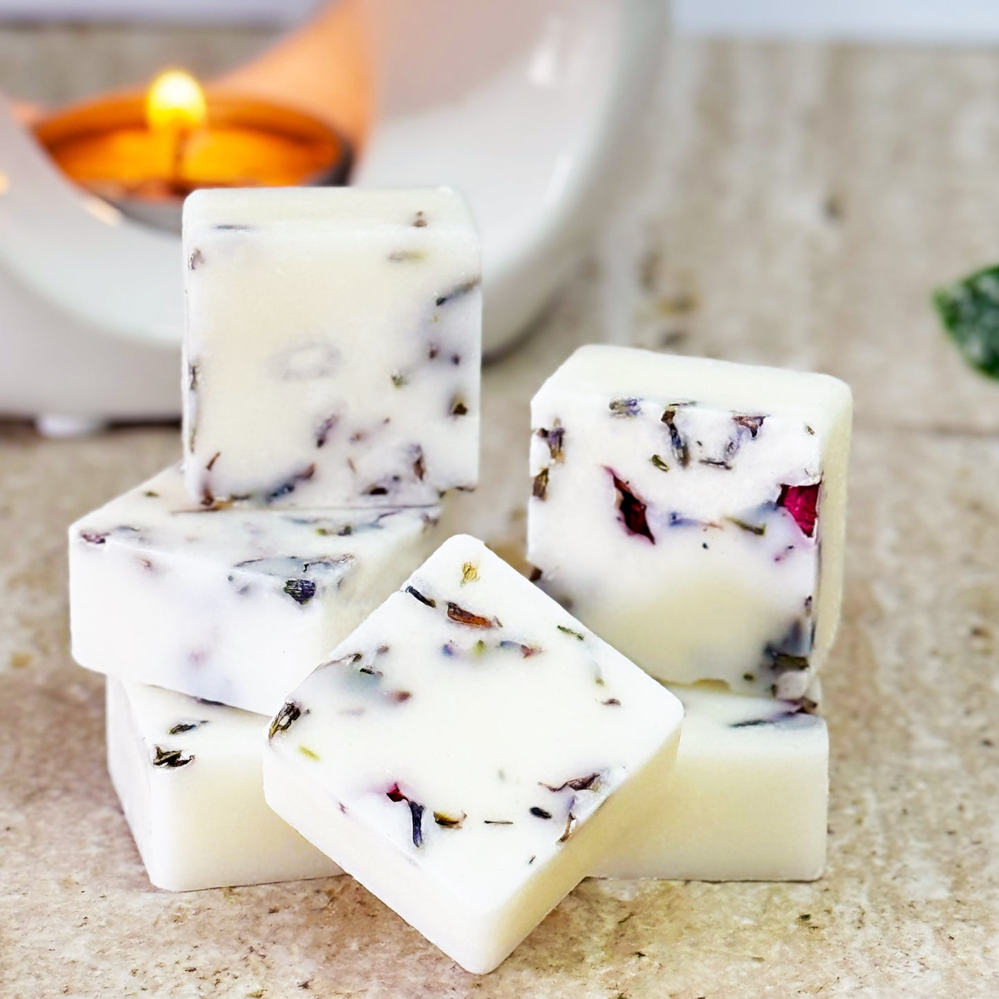 Stacked square botanical wax melts in Blackberry and cedarwood scent, featuring dried lavender and rose petals. The wax melts are displayed on a marble surface with a lit wax warmer in the background.