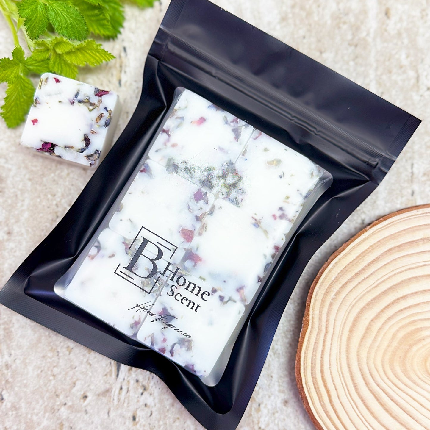 Botanical Blackberry Frost & Cedarwood Wax Melt Bar with Dried Petals in Black Resealable Packaging, Styled with Green Leaves and Wooden Slice