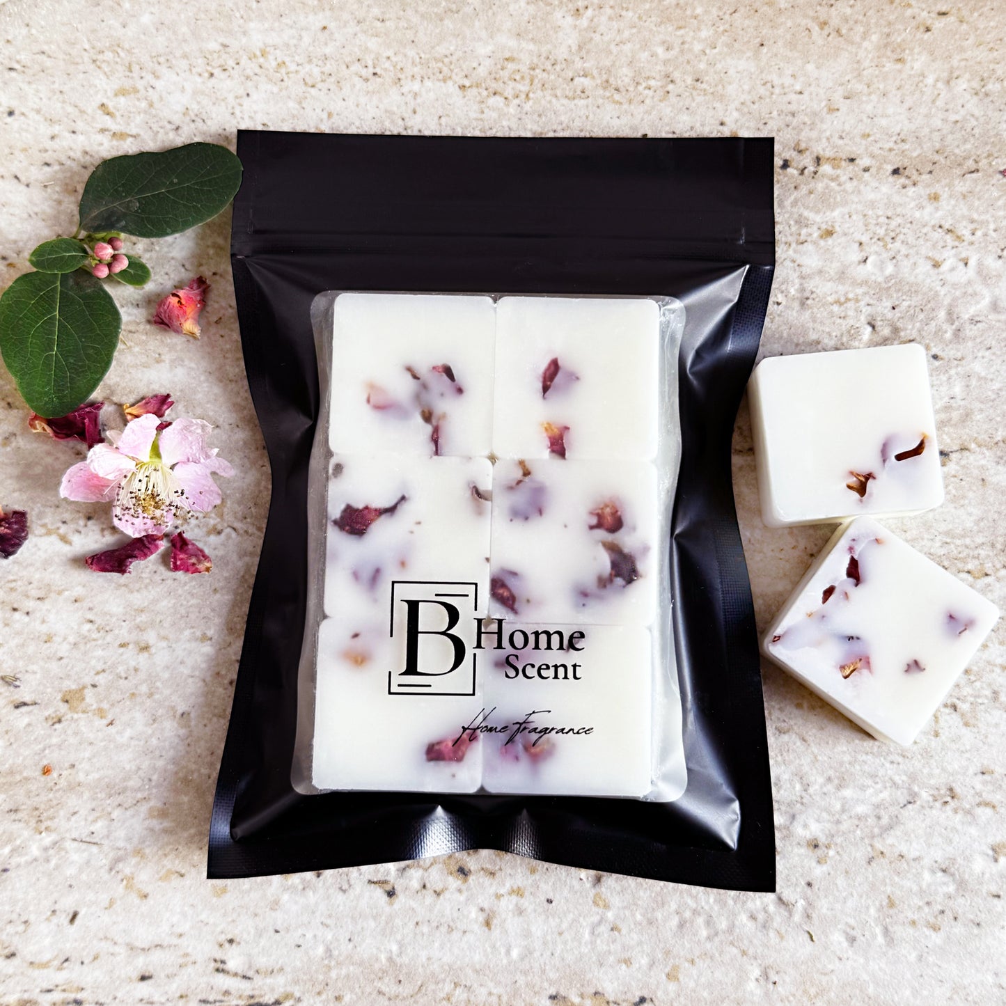 Apple Blossom Prosecco botanical wax melts with dried rose petals, neatly packed in a sleek black bag with the BHOMESCENT logo, placed on a light textured surface with scattered rose petals and green foliage.
