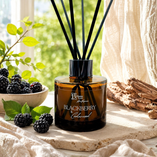 A bottle of Blackberry and  Cedarwood  reed diffuser on a table with blackberries and greenery.