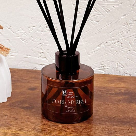 Dark Myrrh and Tonka reed diffuser in amber glass bottle styled on wooden surface