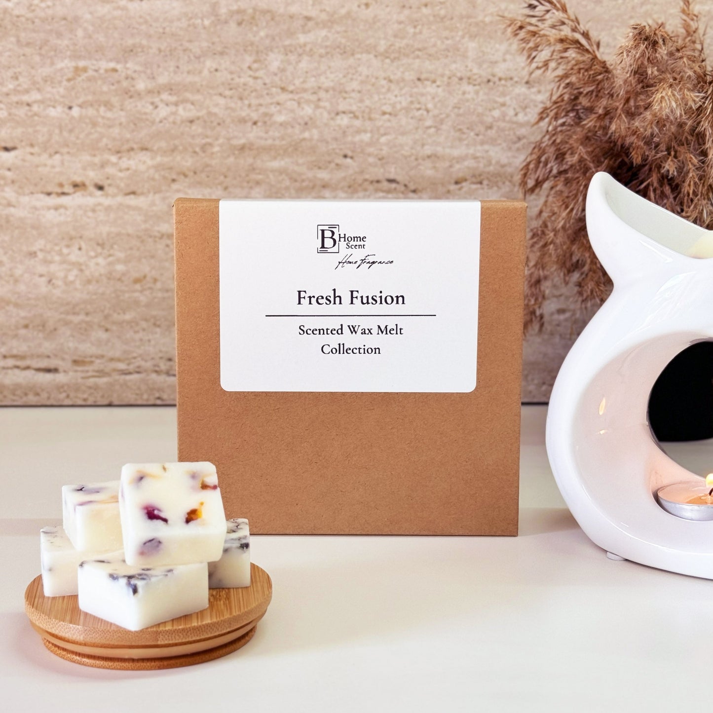 "Fresh Fusion" from the BHomeScent brand. It is a scented wax melt collection, including fresh linen and fresh unstoppables wax melts. The packaging is a simple brown box with a white label. To the left of the box, there are a few wax melt cubes on a wooden plate, which have dried lavender, calendula and rose petals in them. On the right side, there is a white wax melt burner with a lit tealight inside. The overall aesthetic is clean and minimalistic, conveying a fresh and laundry-inspired scent.