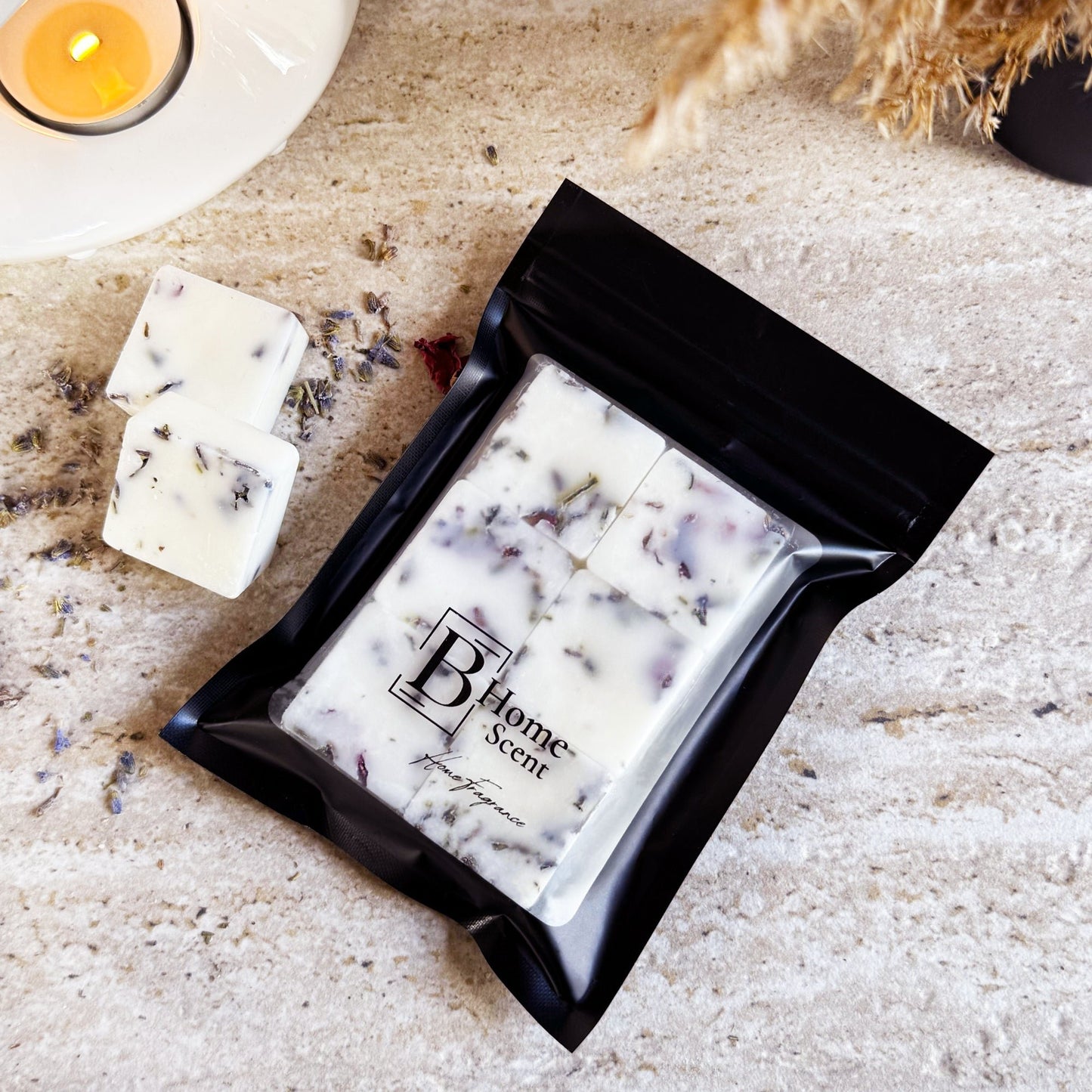 A bag of Blueberry & Jasmin wax melts infused with dried lavender and rose petals. The wax melts are displayed on a light surface, with some loose wax cubes outside the bag. The packaging features the "BHome Scent" label, highlighting the product as a home fragrance.