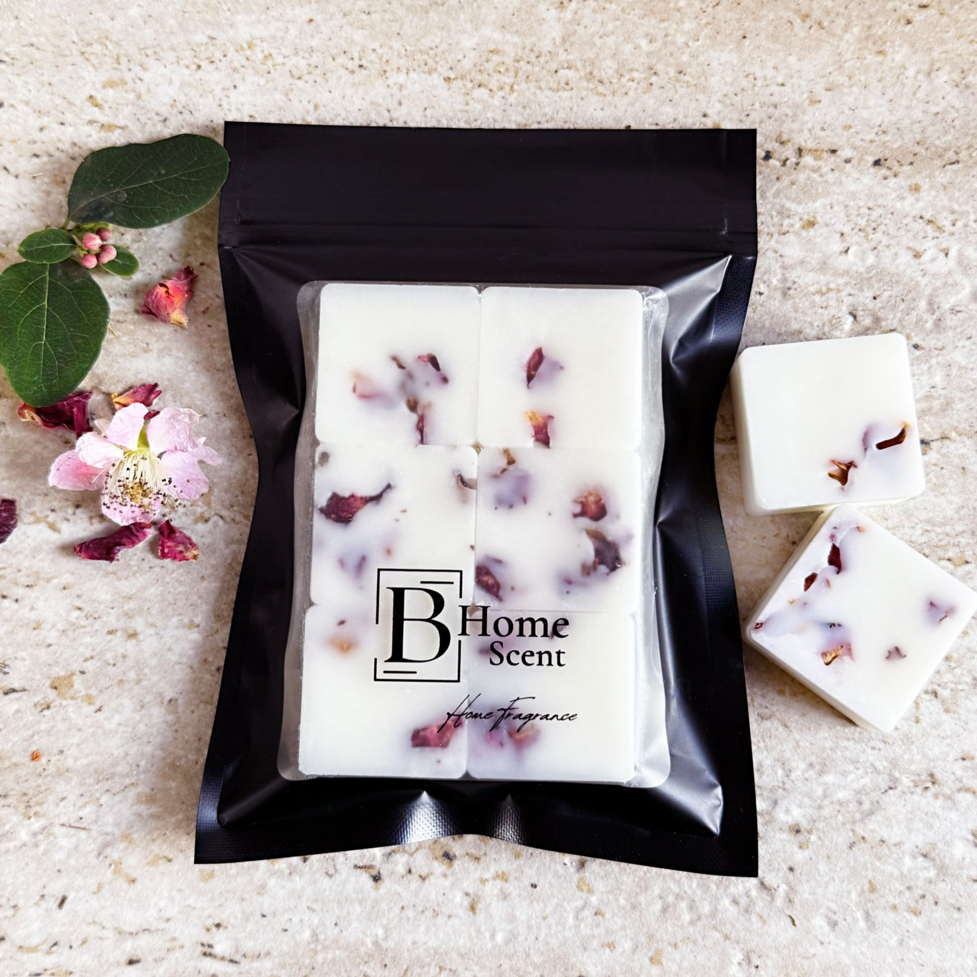 Cherry blossom wax melts with dried rose petals, packaged in a sleek black resealable bag with the 'B Home Scent' logo. The wax melts are white with scattered rose petals, arranged on a beige marble surface with additional rose petals and a small flower nearby.