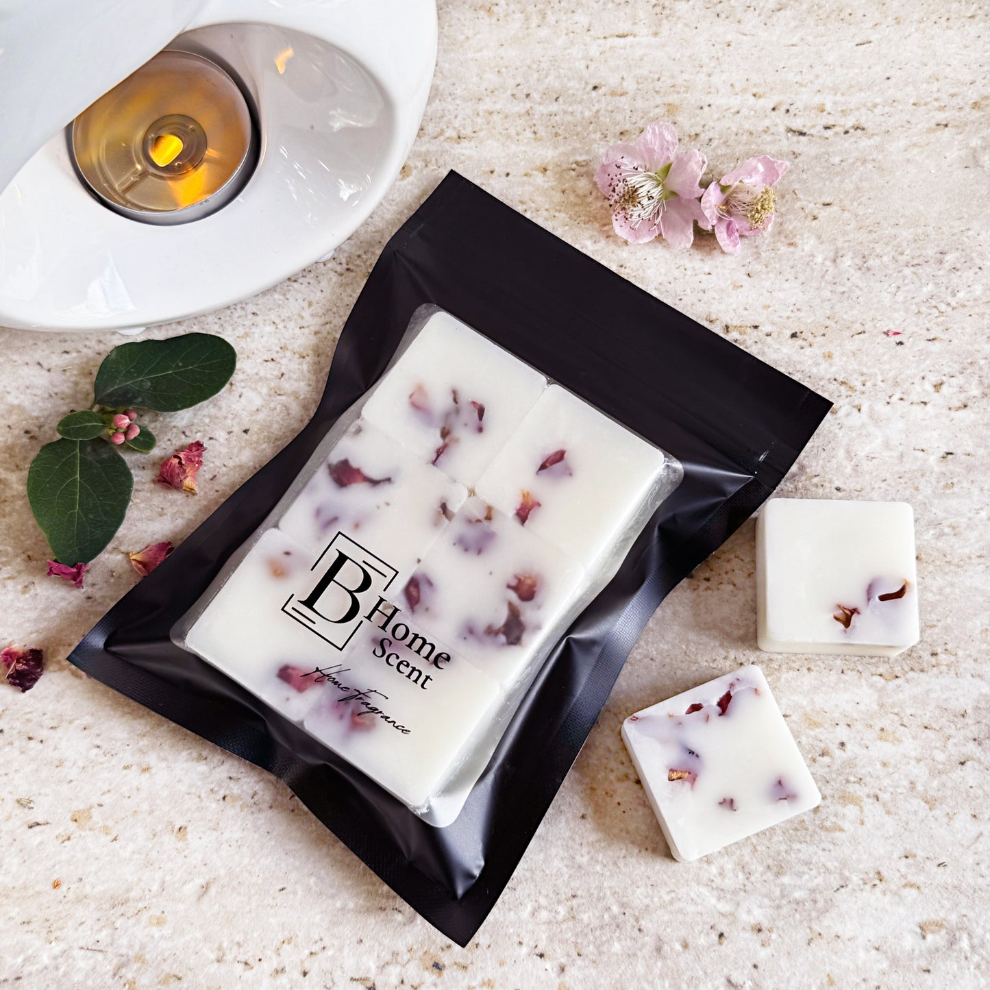 Cherry Blossom wax melts with dried rose petals, packaged in a sleek black resealable bag with the 'B Home Scent' logo. The wax melts are white with scattered rose petals, arranged on a beige marble surface with additional rose petals and a small flower nearby.