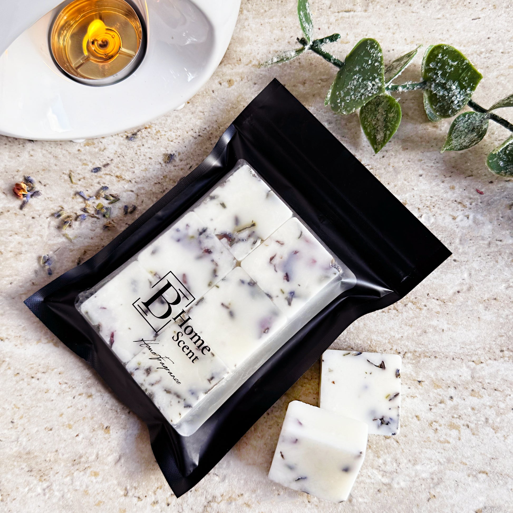 Frosted Eucalyptus wax melts with dried lavender, packaged in a sleek black resealable bag with the 'B Home Scent' logo. The wax melts are white with lavender petals, arranged on a beige marble surface with additional lavender and a frosted eucalyptus.