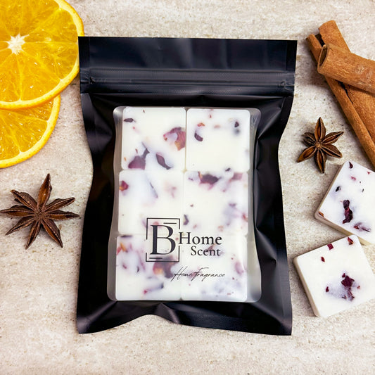 A sealed black pouch labelled 'B Home Scent' containing six mulled wine botanical wax melts with visible floral pieces. The package is surrounded by orange slices, cinnamon sticks, star anise, and additional wax melts.