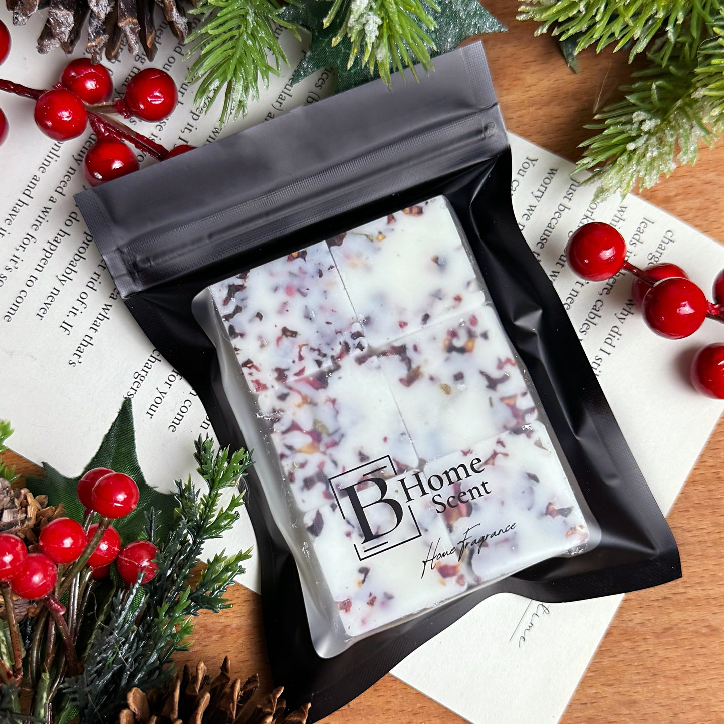 Handcrafted Orange, Cranberry and Cinnamon wax melt snap bar in black zip bag packaging, surrounded by festive greenery and berries.
