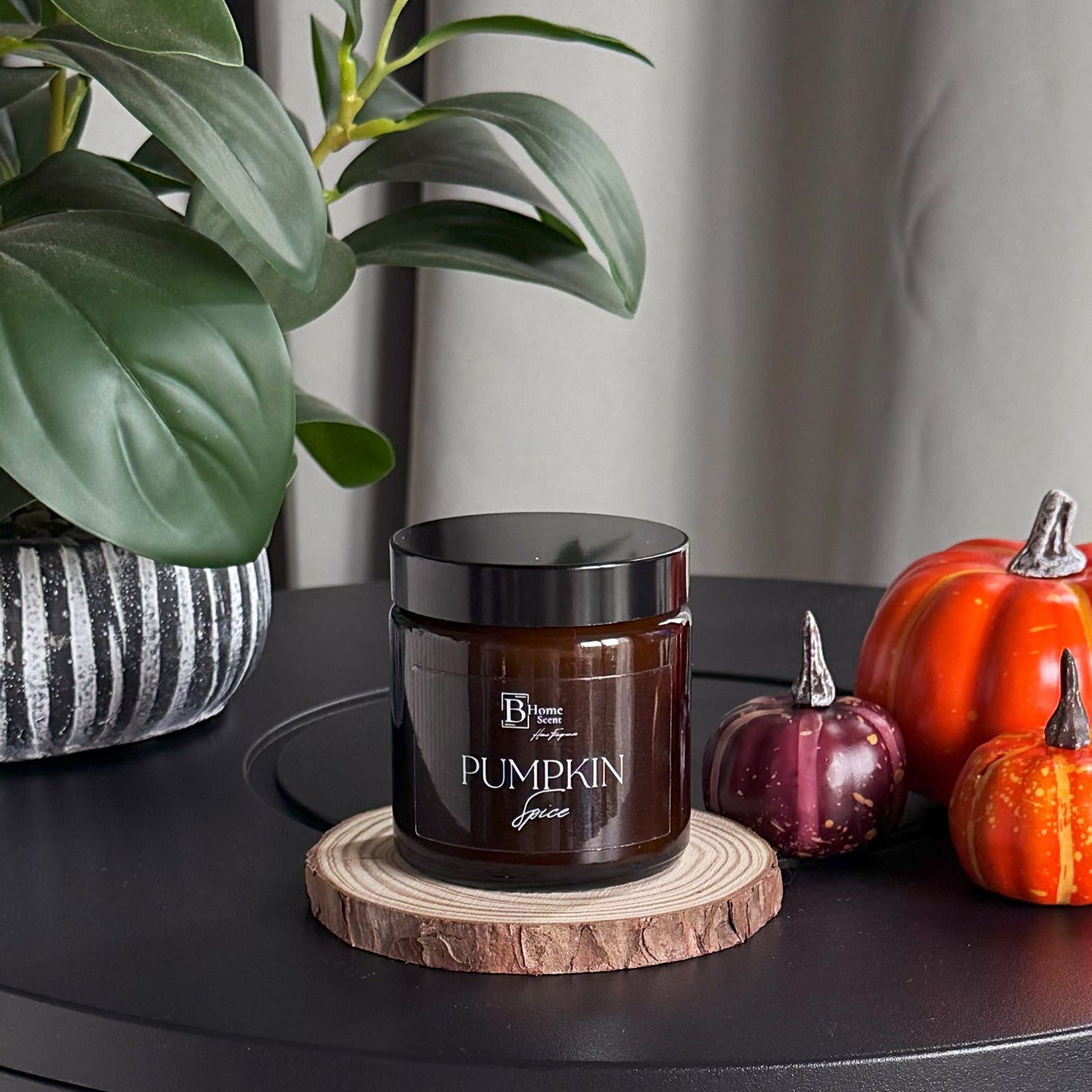 Jar of pumpkin spice on a wooden coaster with decorative pumpkins and a plant in the background.