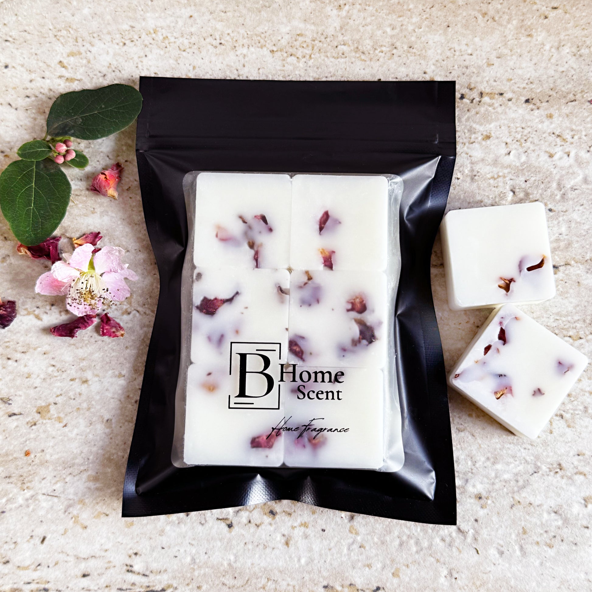 Scarlet Hibiscus botanical wax melts with dried rose petals, neatly packed in a sleek black bag with the BHOMESCENT logo, placed on a light textured surface with scattered rose petals and green foliage.