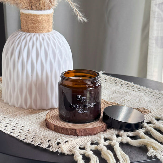 Amber  candle jar labelled 'Dark Honey and Tobacco'  on a textured surface with decorative elements.