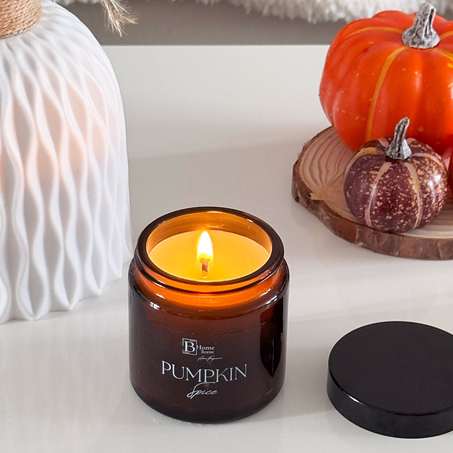 Candle labeled 'Pumpkin Spice' with decorative pumpkins on a white surface