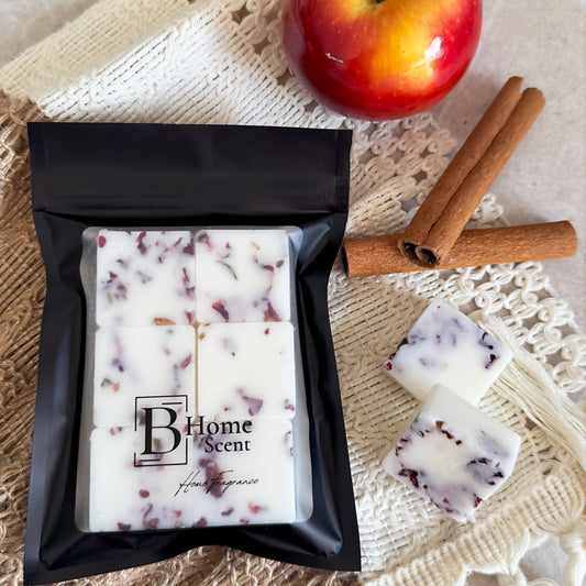 Packaged candles with a cinnamon stick and apple on a textured surface