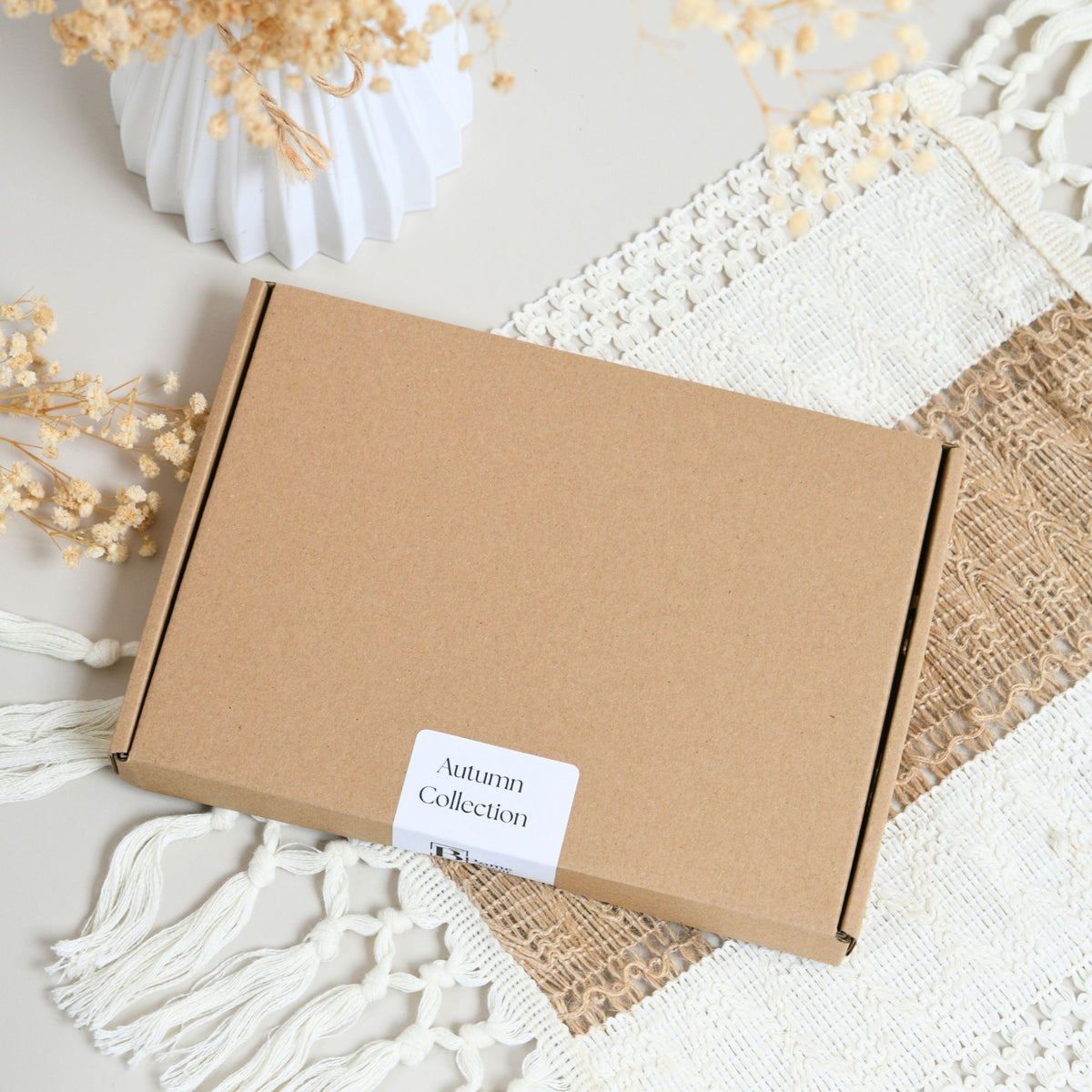 Autumn Wax Melt Snap Bar, A flat brown kraft cardboard box with a white label reading 'Autumn Collection,' styled on a cream textile with tassels and dried floral decor.