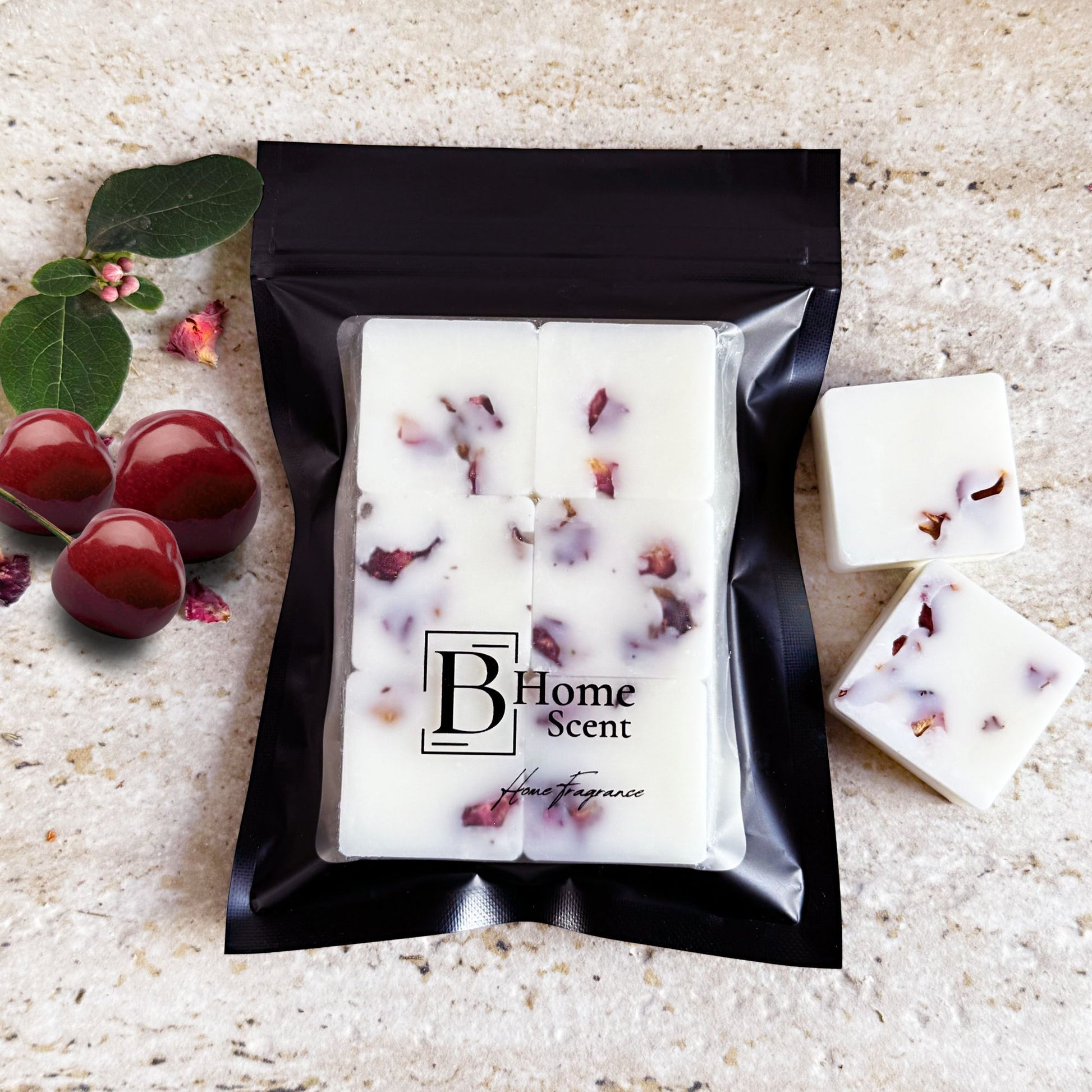 Black Cherry botanical wax melts with dried rose petals, displayed in a sleek black resealable bag. Two wax melt cubes are placed beside the bag, showcasing the embedded rose petals. A lit wax burner and fresh cherries with green leaves are also visible on a light marble surface, creating an elegant and inviting presentation.