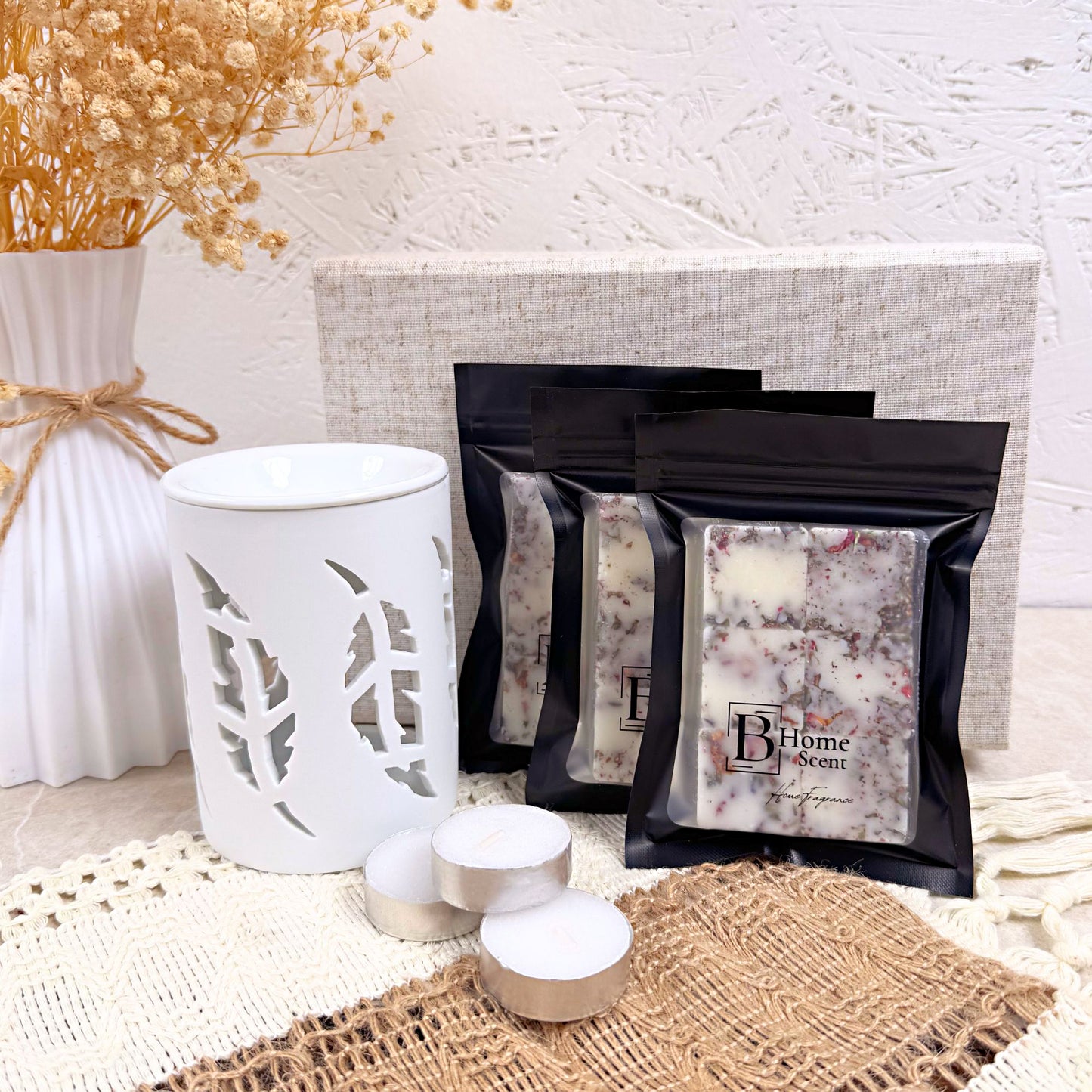 wax melt burner, tealights, and black bags with botanical wax melts on a textured surface.