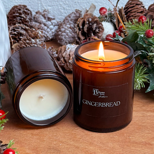 Amber jar gingerbread scented candle lit on a wooden surface with pinecones and festive greenery.