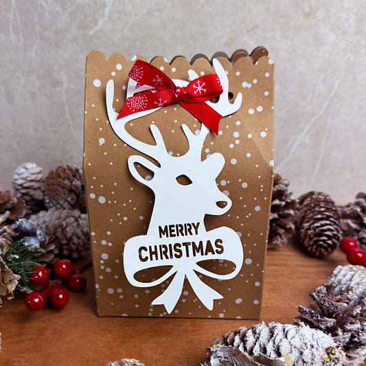 wax melt advent calendar with reindeer design and red bow, surrounded by pine cones and berries.