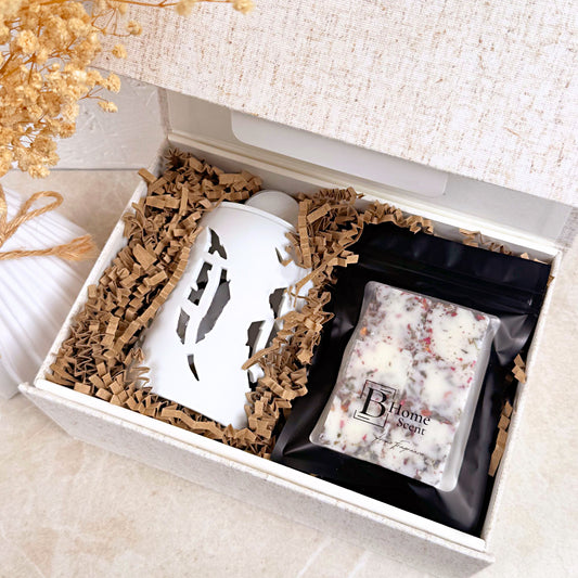 Gift box with a white wax melt burner and a bags of wax melts on a light surface.