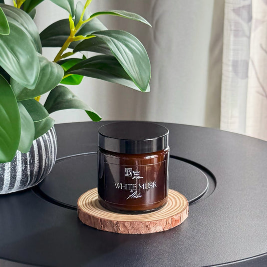 amber candle jar of 'White Musk' on a wooden coaster with a plant in the background